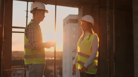 Slow-motion-of-two-engineers-are-talking-about-the-future-project-for-the-construction-of-a-skyscraper-business-center-and-shaking-hands-at-sunset.